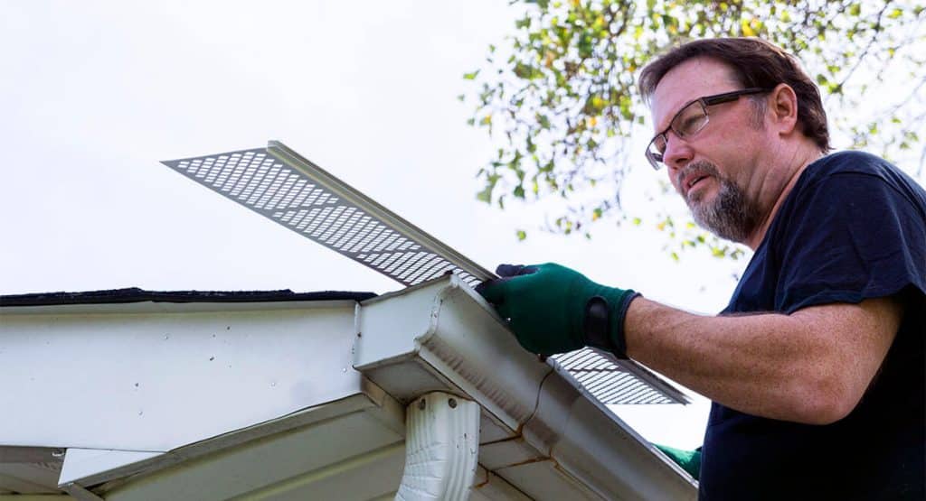 roofing contractor installing rain gutter guards to gutter system on home