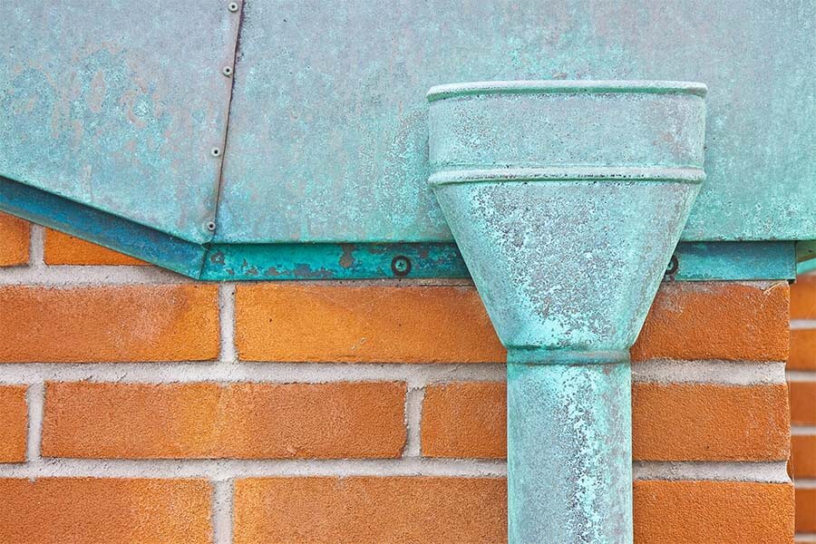 copper leader head with aged patina coat for gutter system installed on monterey california home