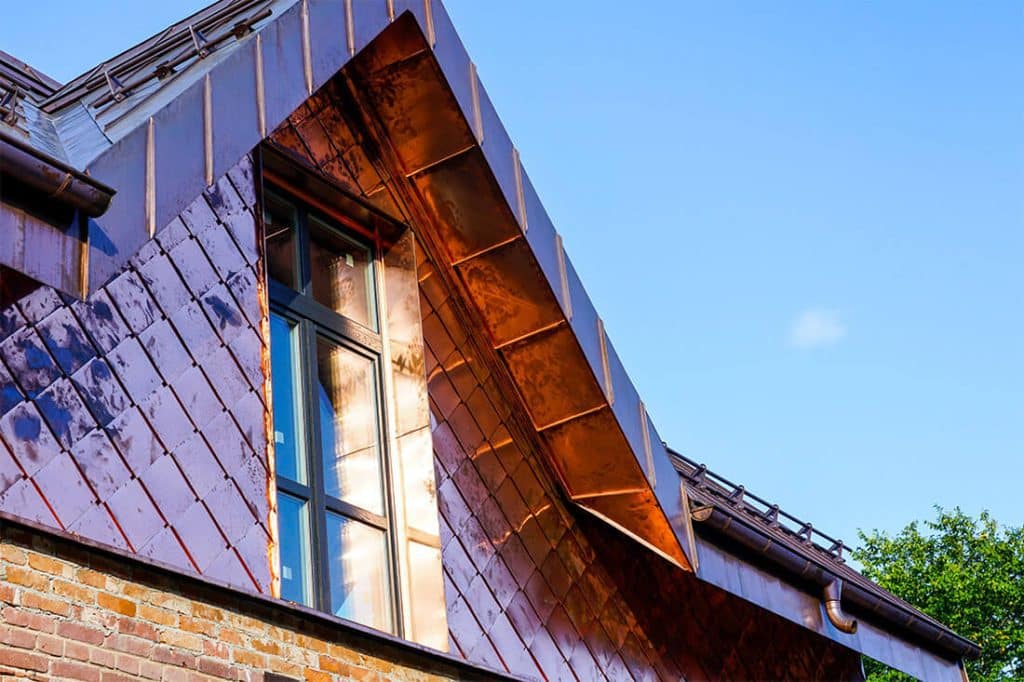 Close-up view of a modern home with a custom copper-clad dormer and diamond-pattern copper siding, reflecting sunlight against a clear blue sky