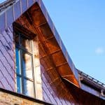 Close-up view of a modern home with a custom copper-clad dormer and diamond-pattern copper siding, reflecting sunlight against a clear blue sky