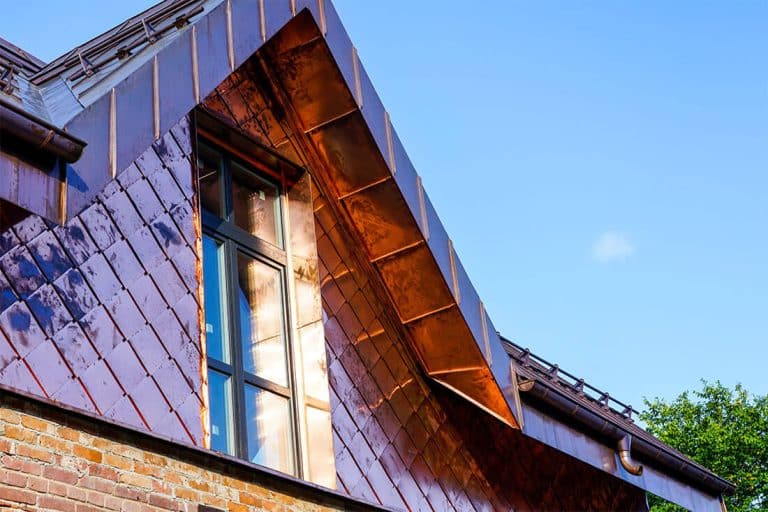 Close-up view of a modern home with a custom copper-clad dormer and diamond-pattern copper siding, reflecting sunlight against a clear blue sky